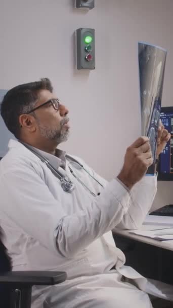 Inyección vertical media del ortopedista indio maduro que sostiene la resonancia magnética del pie, analizando y detectando atentamente anormalidades o estudiando lesiones - Metraje, vídeo