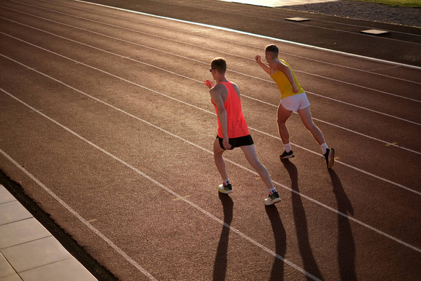 Két sportoló fut egy stadionban naplementekor. - Fotó, kép