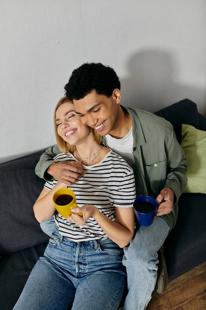 A young interracial couple relaxes on a couch in a modern apartment, sharing coffee and a cozy moment together. - Foto, Bild
