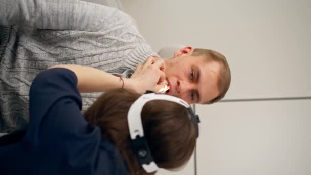 診療所の垂直ビデオクローズアップ若い医師の喉の鼻は患者の喉を検査する - 映像、動画
