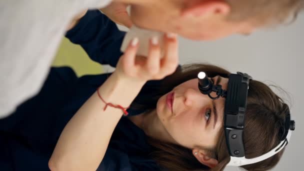 診療所の垂直ビデオクローズアップ若い医師の喉の鼻は患者の喉を検査する - 映像、動画