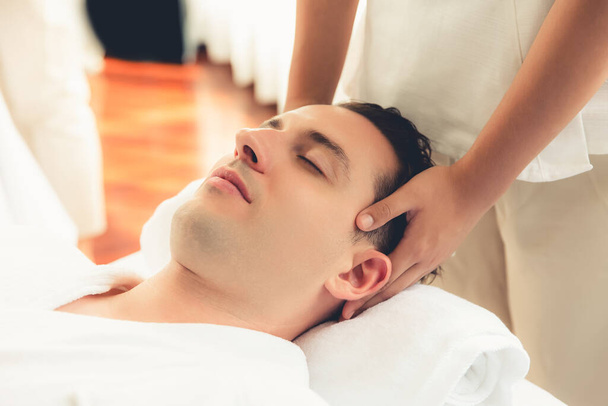 Kaukaski mężczyzna korzystających relaksujący antystresowy masaż głowy i rozpieszczające piękno twarzy rekreacji rekreacji skóry w dayspa nowoczesne światło ambient w luksusowym ośrodku lub hotelowym salonie spa. Cichy zapach - Zdjęcie, obraz