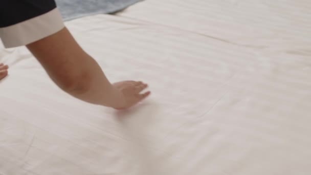 Przycięty strzał nierozpoznawalnej pokojówki wygładzającej białą pościel hotelową na łóżku dłońmi podczas przygotowywania pokoju dla gości rano - Materiał filmowy, wideo