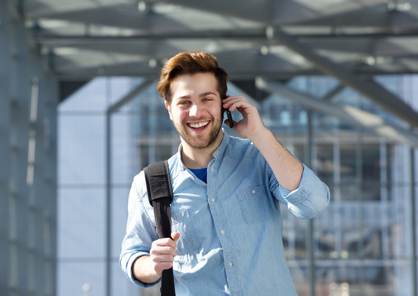 Happy young man with bag talking on cell phone - Photo, Image