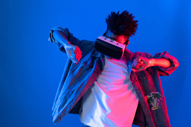 Mosolygó fiatal afro-amerikai nézi át a VR tánc dalban hologram játék rózsaszín kék neon fal metaverse világ összekötő digitális futurisztikus technológia virtuális valóság. Vállalkozás. - Fotó, kép