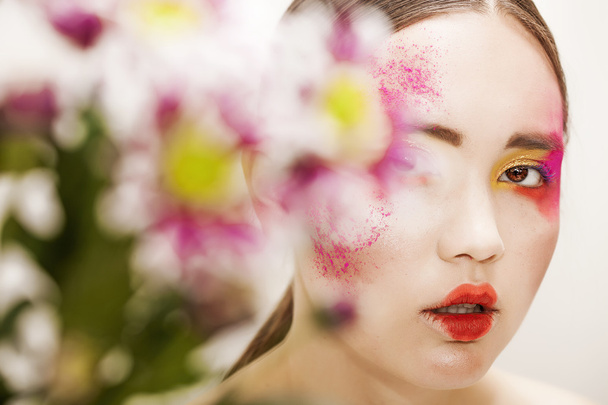 Портрет девушки с красочным макияжем и размытыми цветами
 - Фото, изображение