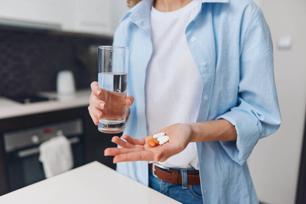 Nainen tilalla lasi vettä ja pilleri kädessä seisoo keittiön laskuri, terveydenhuollon käsite - Valokuva, kuva