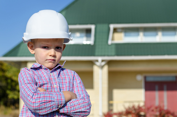 Poika yllään kova hattu esittää valmiin talon
 - Valokuva, kuva