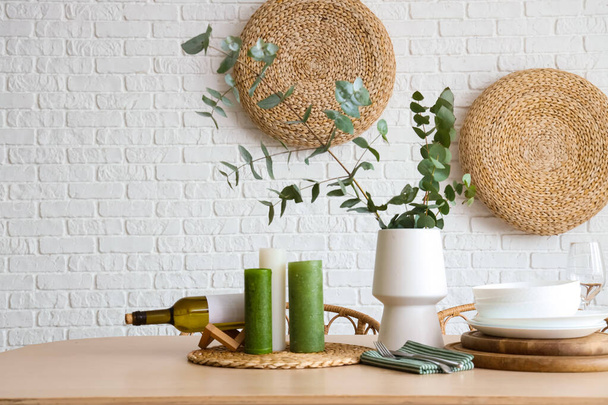 Vase with eucalyptus branches, plates and candles on dining table in room - Photo, Image