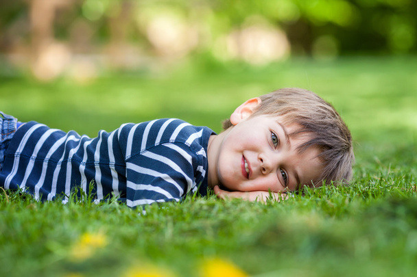 Smiling little boy lying on the grass in the park - Fotografie, Obrázek