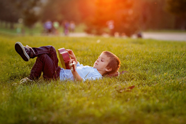 Adorable boy with guitar, sitting on the grass - Fotografie, Obrázek