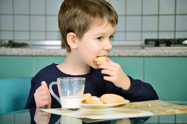 El niño muerde galletas, sentado en la mesa. horizontales
 - Foto, imagen