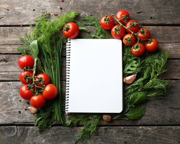 Open recipe book with fresh herbs, tomatoes and spices on wooden background - Photo, image