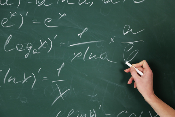 Female hand writing formulas on blackboard with chalk, close up - Фото, изображение