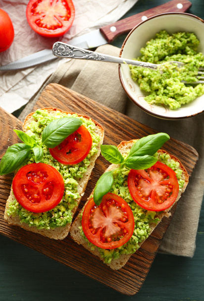 Sandwich vegano con aguacate y verduras sobre tabla de cortar, sobre fondo de madera
 - Foto, Imagen