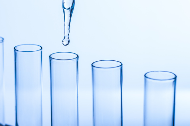 laboratorium Pipetteer met druppel vloeistof over glas reageerbuisjes  - Foto, afbeelding
