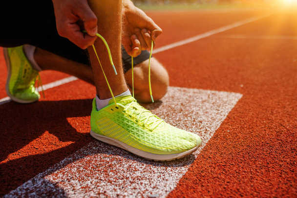 Um atleta está amarrando sapatos de corrida de néon amarelo brilhante em uma pista, se preparando para uma corrida de nascer do sol - Foto, Imagem