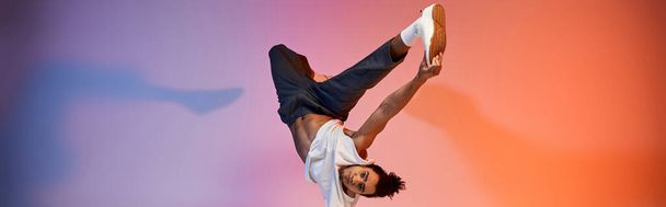 Un jeune homme afro-américain danse sur un fond de gradient vibrant, mettant en valeur ses compétences acrobatiques et son expression énergique. - Photo, image