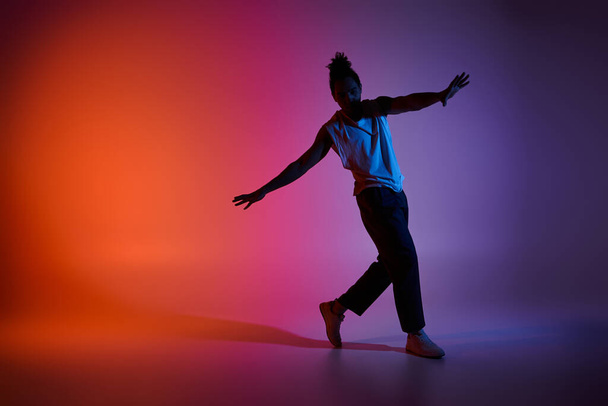 Un joven afroamericano baila con energía y gracia sobre un vibrante fondo de gradiente. - Foto, imagen