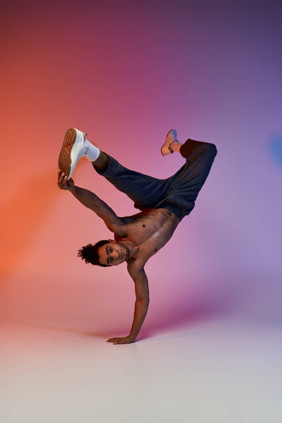 Een jonge Afro-Amerikaanse man is gefotografeerd het uitvoeren van een handstand dansbeweging op een kleurrijke gradiënt achtergrond. - Foto, afbeelding