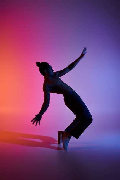 Silueta mladého Afroameričana tančícího proti růžovému a purpurovému pozadí. - Fotografie, Obrázek