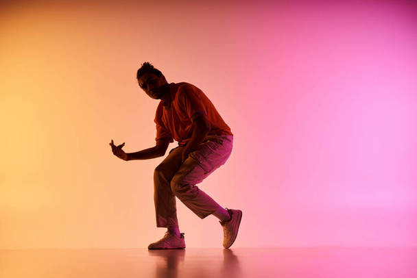 Een jonge Afro-Amerikaanse mannelijke danser voert een beweging op een kleurrijke gradiënt achtergrond. - Foto, afbeelding