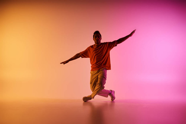 Un joven afroamericano con una camisa naranja baila sobre un colorido fondo degradado. - Foto, imagen