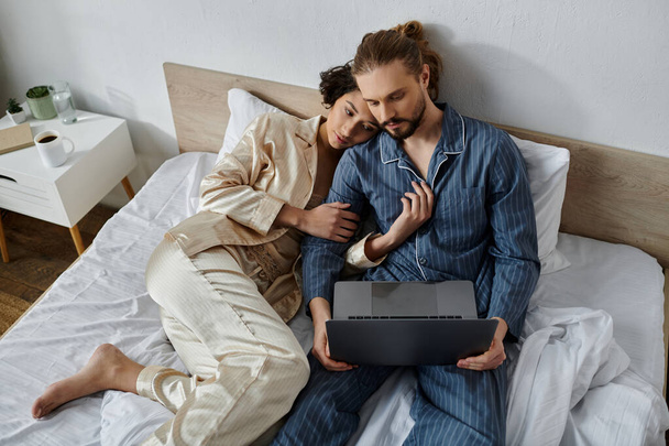 Un couple en pyjama se détend au lit ensemble, avec l'homme utilisant un ordinateur portable. - Photo, image