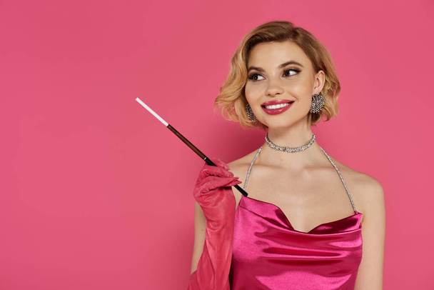 Woman in pink satin dress smiles with cigarette against pink background. - Photo, Image