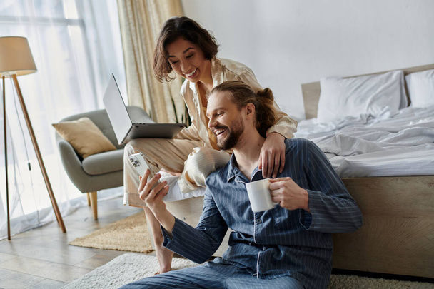 Una pareja cariñosa se relaja en casa, compartiendo una taza de café y un portátil. - Foto, imagen