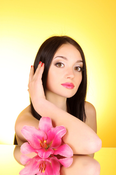 Beautiful young woman with lily flower on yellow background with - Foto, Imagen