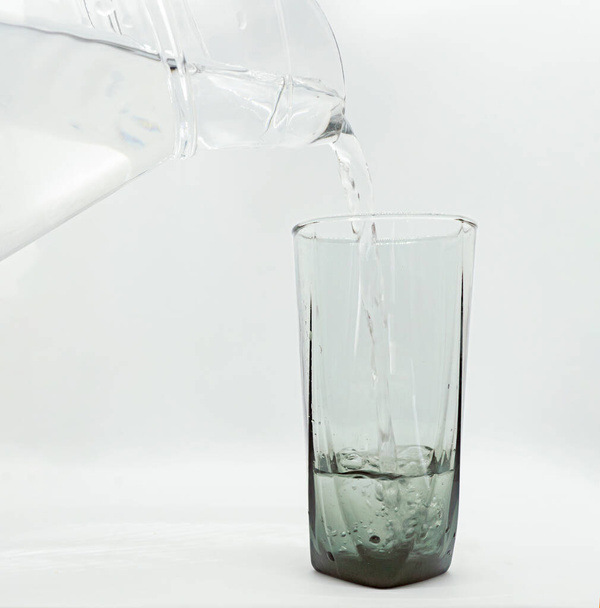 szklany dzbanek i szklaną filiżankę obok wylewa schłodzoną wodę odizolowane białe tło png - Zdjęcie, obraz