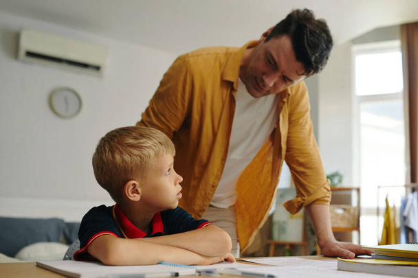 Pai falando com seu filho sobre estudo enquanto ele faz lição de casa - Foto, Imagem