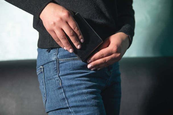 Młoda biała kobieta wkłada portfel do kieszeni dżinsów. - Zdjęcie, obraz