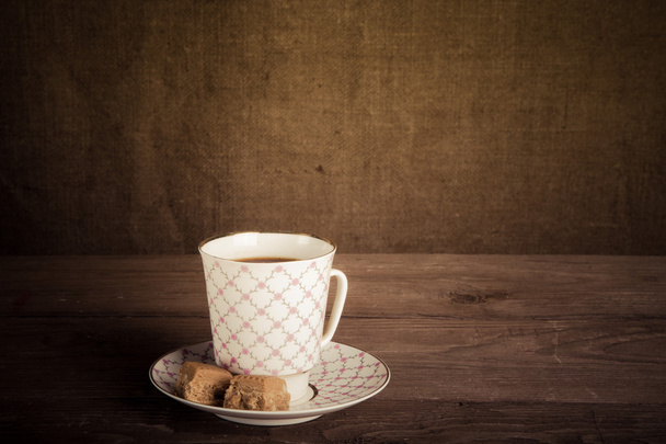 Porcelain cup of coffee with toffee on old wooden table against  - Foto, afbeelding