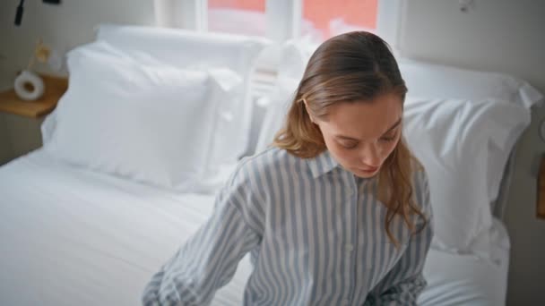 Woman in bedroom reflecting thoughts with sad expression closeup. Upset lady in striped pajama sitting on comfortable bed at morning. Sad girl feeling loneliness in tranquil apartment atmosphere. - Imágenes, Vídeo
