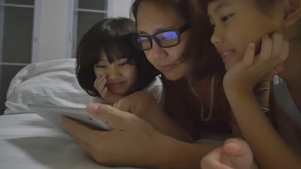 Азиатская мама лежит со своими дочерьми и играет с цифровой планшет вместе
 - Кадры, видео