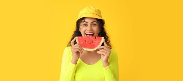 Happy young African-American woman with slice of fresh watermelon on yellow background   - Photo, Image