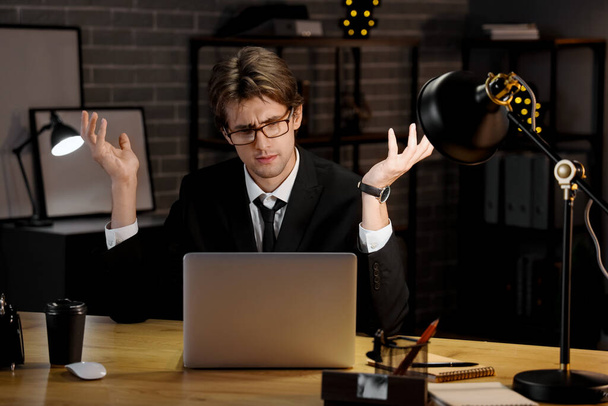 Displeased young businessman working in office at night - 写真・画像
