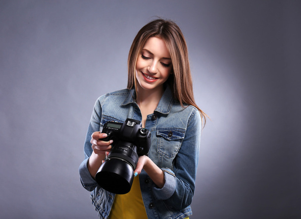 Young female photographer taking photos on grey background - Foto, afbeelding