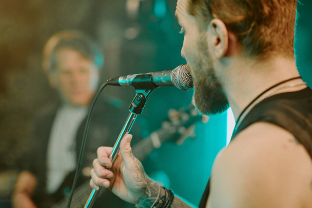 Primer plano del joven vocalista caucásico cantando una canción de heavy metal en el micrófono en el escenario - Foto, Imagen