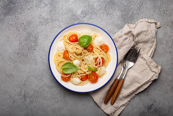 Heerlijke en verse spaghetti met kerstomaten en mozzarella kaas, op smaak gebracht met peper en basilicum, geserveerd op een bord, kopieerruimte - Foto, afbeelding