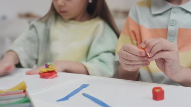 Midsection de menino e menina pré-escolar caucasiano sentado à mesa diligentemente criando formas de argila modelagem colorida durante a aula de arte no jardim de infância - Filmagem, Vídeo
