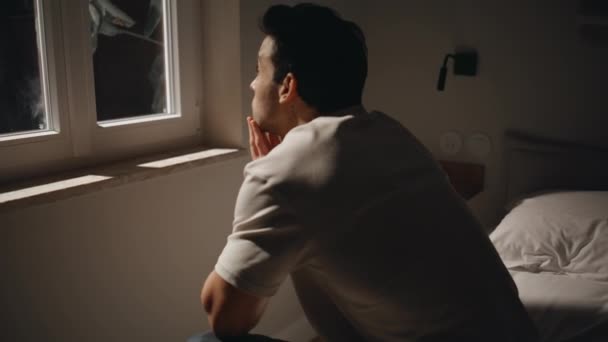 Egy férfi, aki éjjeli ablakot néz, depressziósnak érzi magát. Kimerült fickó ül az ágyban, aggódik az élet gondjai miatt éjfélkor. Aggódó férfi érzés magány szenved álmatlanság sötét szobában. - Felvétel, videó