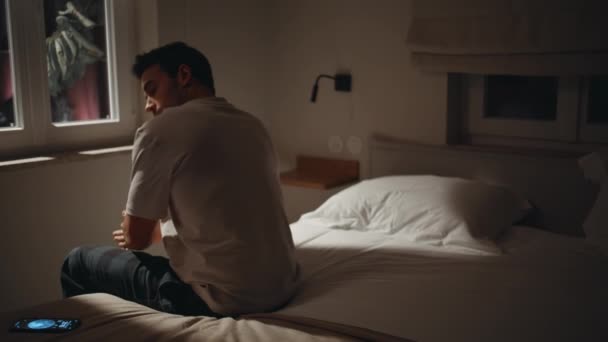 Lonely man sitting midnight bedroom with smartphone. Unhappy guy feeling sadness at night absorbed in cellphone. Addicted male putting mobile phone on bed suffering from insomnia. Depression concept. - Felvétel, videó