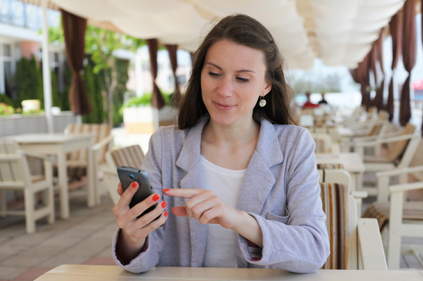 Tyttö käyttää älypuhelinta ravintolan terassilla
 - Valokuva, kuva