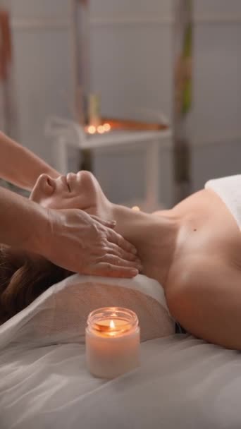 Spokojna scena profesjonalnej terapii masażu szyi w spokojnym otoczeniu spa. Klient leżący na łóżku do masażu z białym ręcznikiem, otoczony kojącą atmosferą świec, promującą relaks. - Materiał filmowy, wideo
