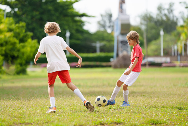 サッカーをする子供. 子供たちは屋外のピッチでサッカーをする. サマーパークでボールを蹴る少年. 幼児のための健康的な活動. スクールスポーツクラブチーム. サッカージュニアリーグ. - 写真・画像