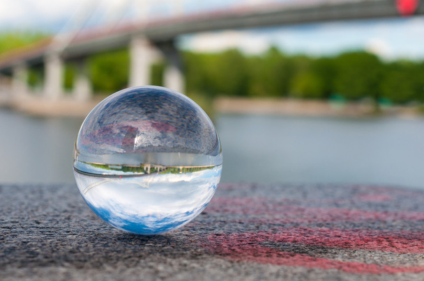 Bola transparente de vidrio sobre fondo de puente y superficie granulada. Con espacio vacío
 - Foto, Imagen
