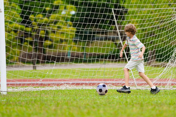 Lapsi pelaa jalkapalloa. Lapset pelaavat jalkapalloa ulkokentällä. Pikkupoika potkii palloa kesäpuistossa. Terveellistä toimintaa pienille lapsille. Koulun urheiluseuran joukkue. Jalkapallo juniori liiga. - Valokuva, kuva